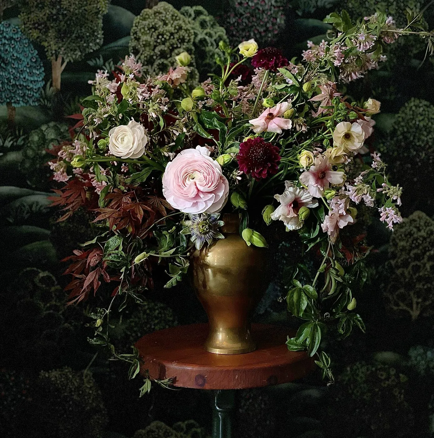 Ranunculus, scabiosa, and trailing passion vine in a brass urn