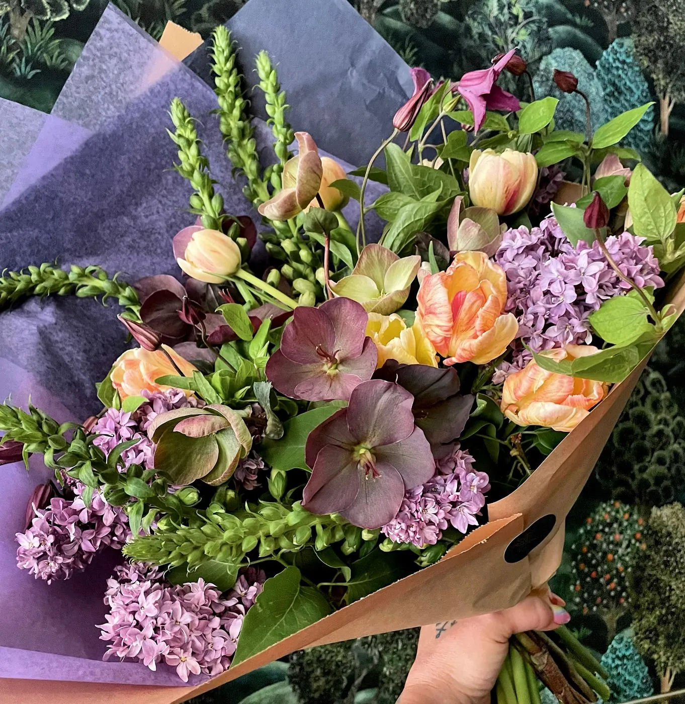 Hand-tied bouquet of lilac, tulips, and hellebore in kraft paper wrap