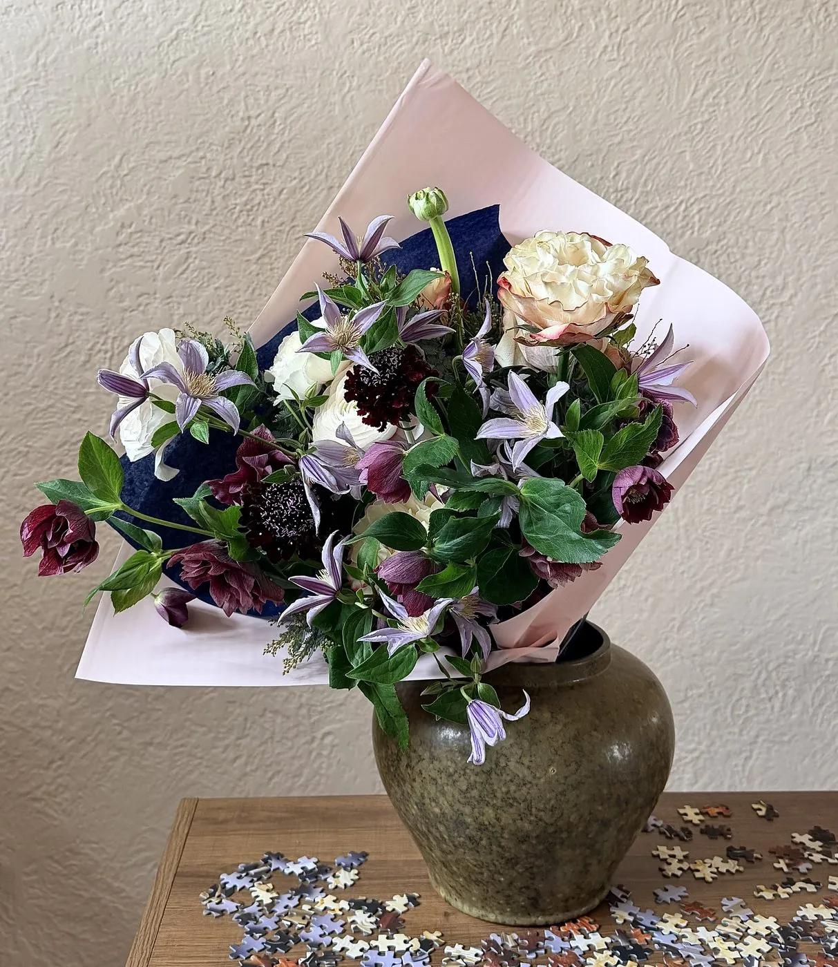 Wrapped bouquet of clematis, hellebore, and ranunculus in a stoneware vase