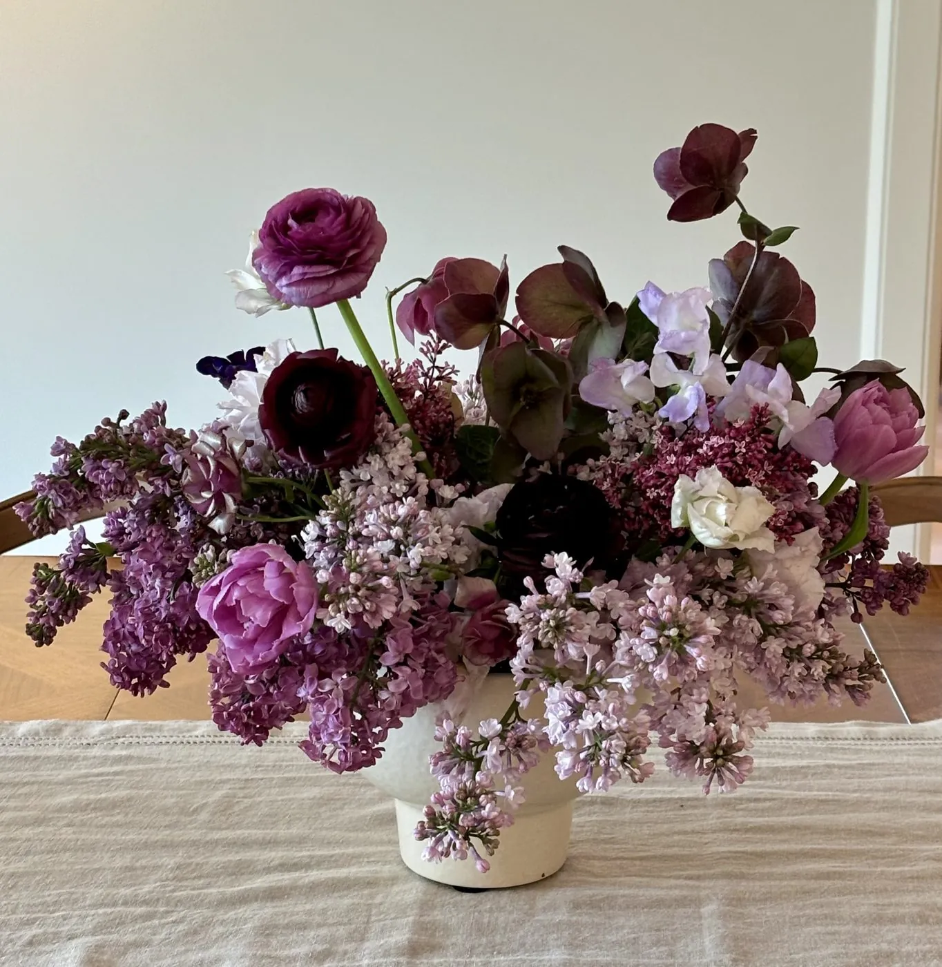 Lilac, tulips, and hellebore centerpiece in a white footed vessel
