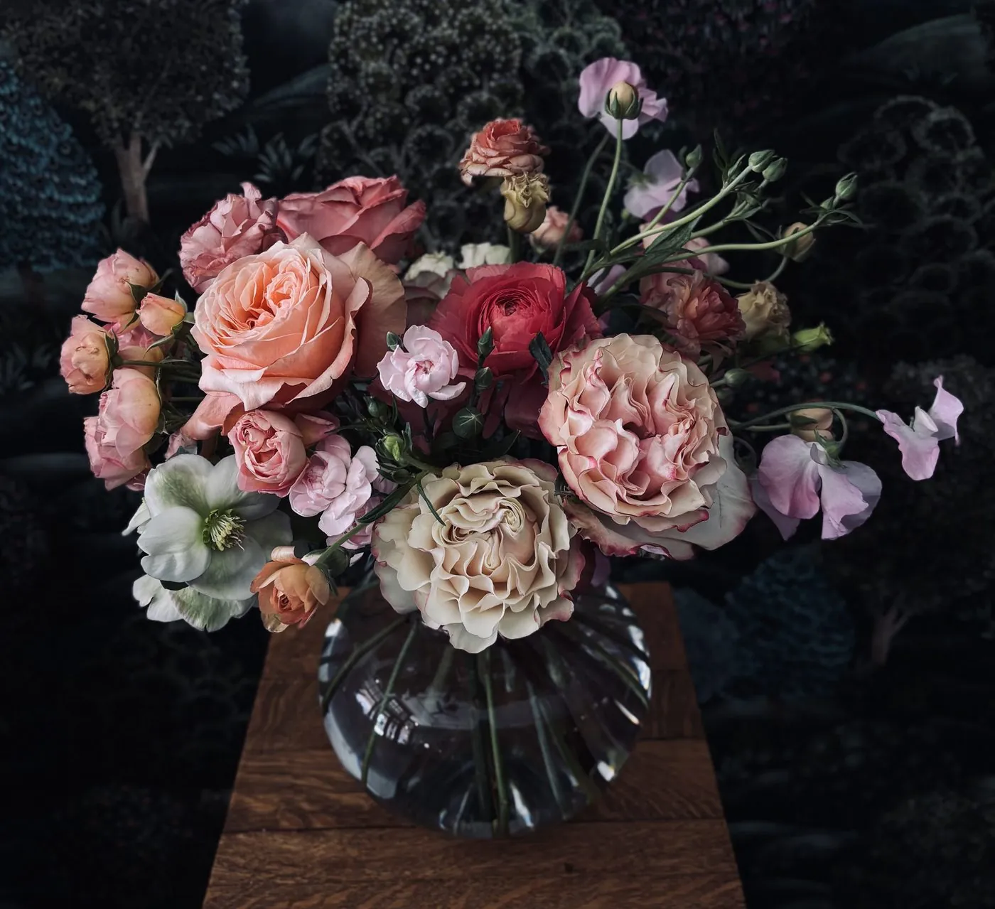 Peach garden roses and carnations in a glass vase at nightfall